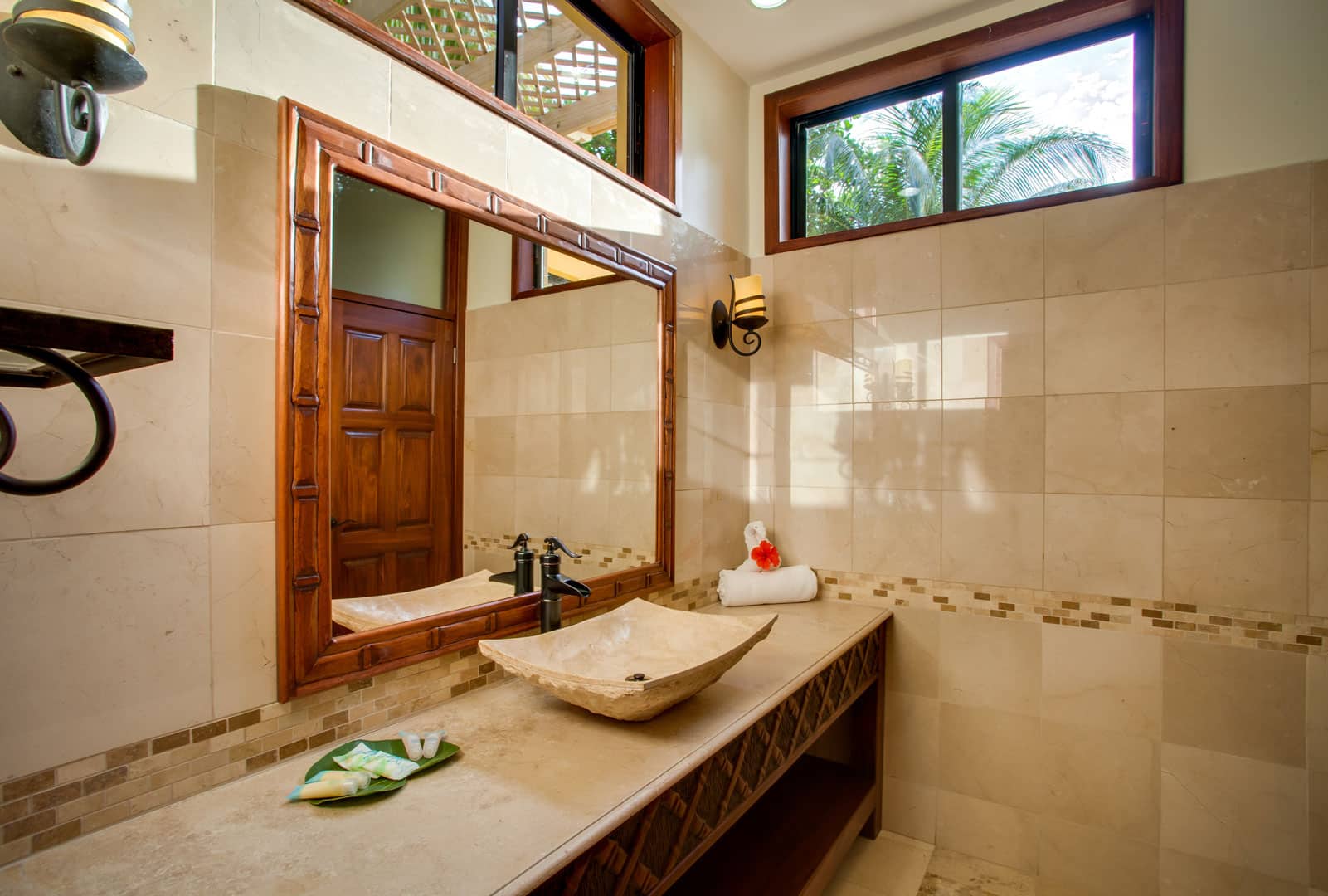 The bathroom with a large vanity mirror, a tiled counter-top and sink inside the Villa Margarita Beachfront Deluxe Rooms at The Resort at Almond Beach