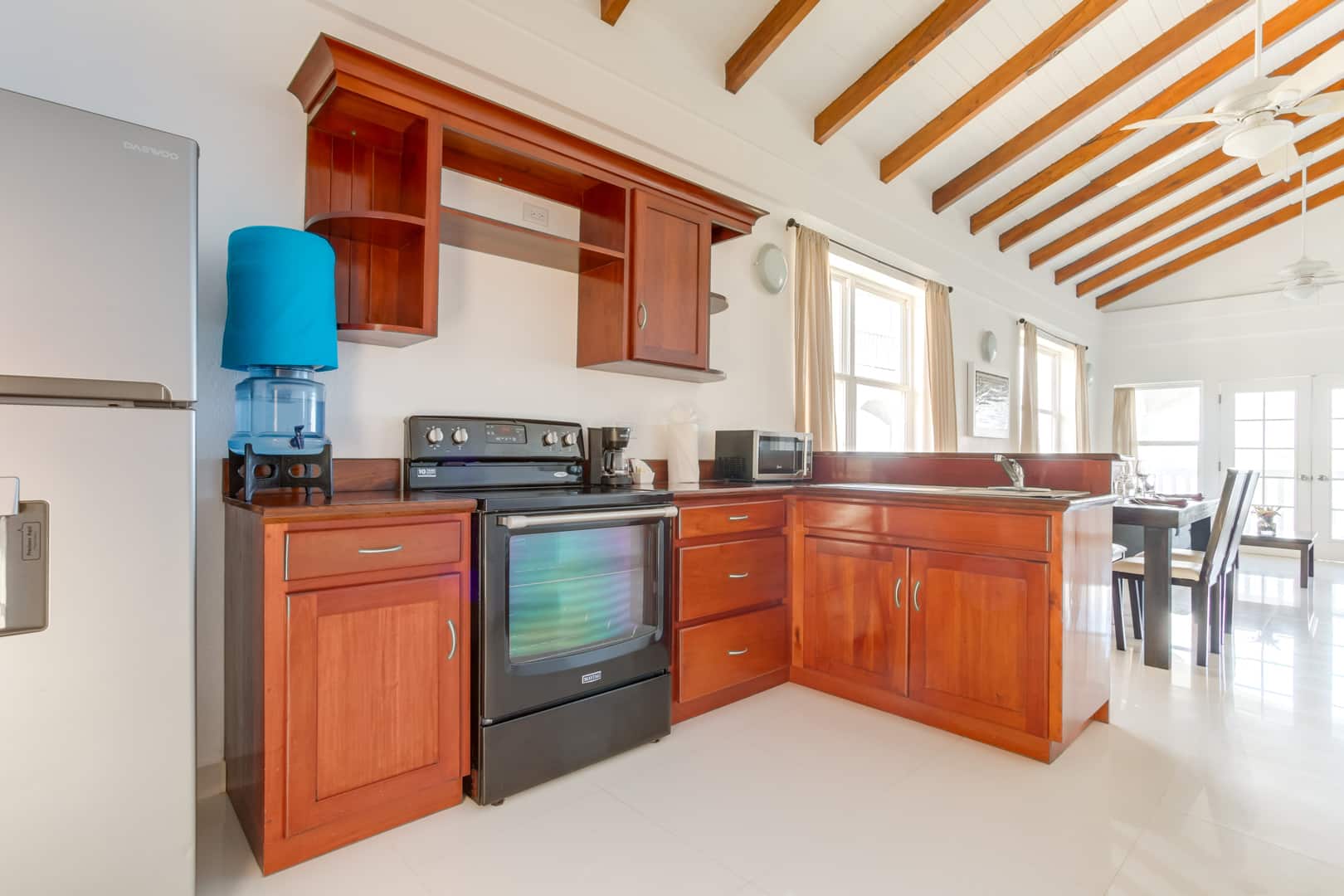 The kitchen with varnished wooden cabinets, a water dispenser, a black stove and a grey refrigerator inside the 2 Bedroom Lagoon Bayview at Umaya Resort & Adventure