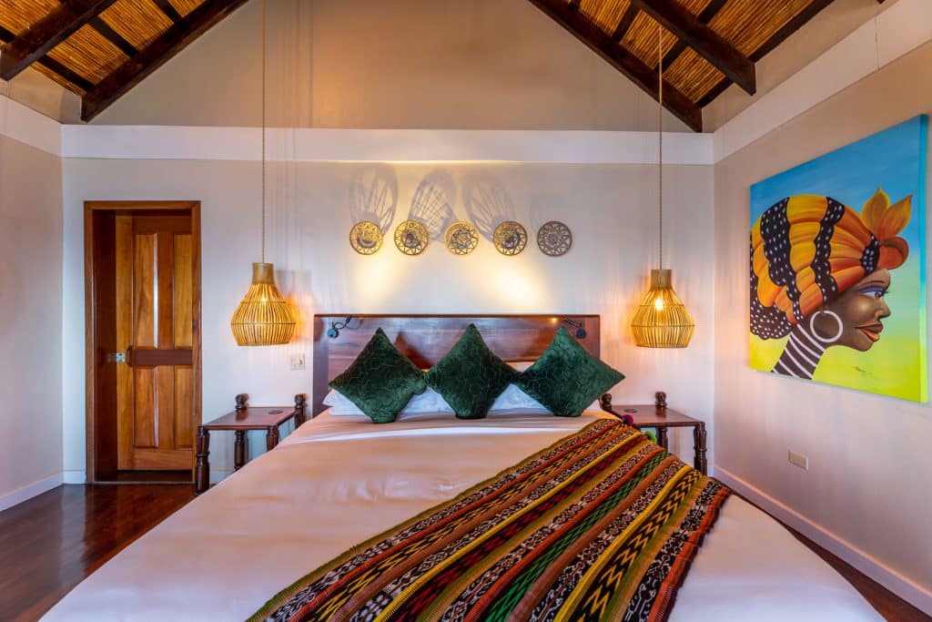 Master bedroom with a bed with pillows and linen and two lamps inside the Beachfront Cottages at The Resort at Almond Beach