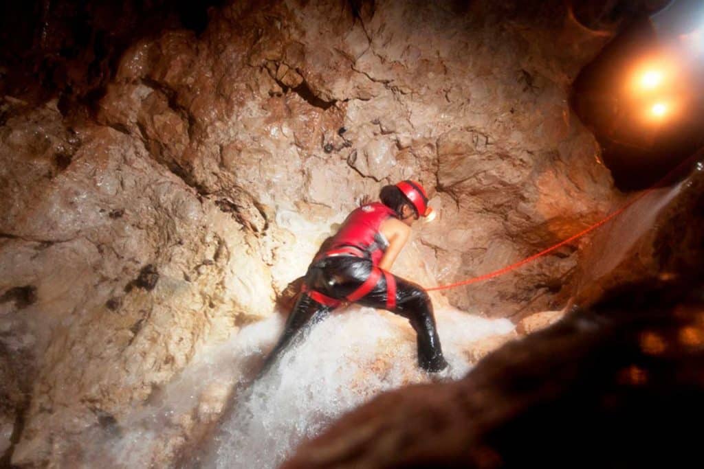 A guest climbing up a waterfall on the waterfall cave expedition at The Rainforest Lodge at Sleeping Giant Resort