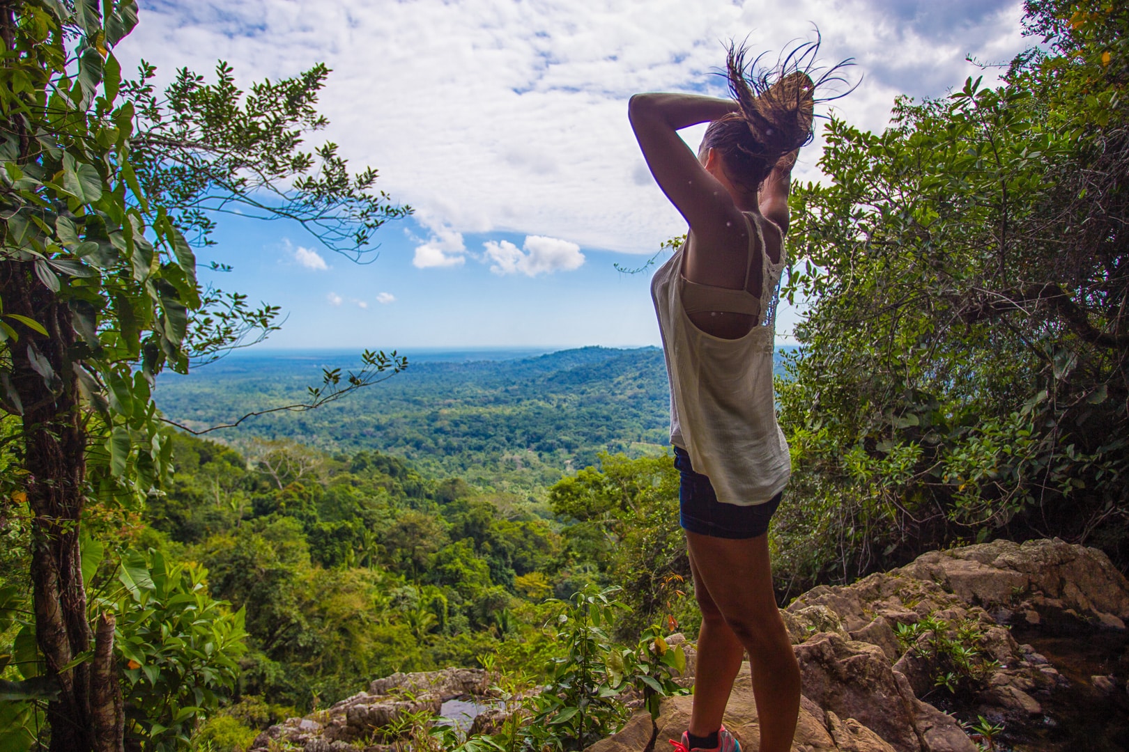 A guest standing the edge of a cliff overlooking the mountains and rainforest on the Mayflower Waterfall Hiking at The Lodge at Jaguar Reef