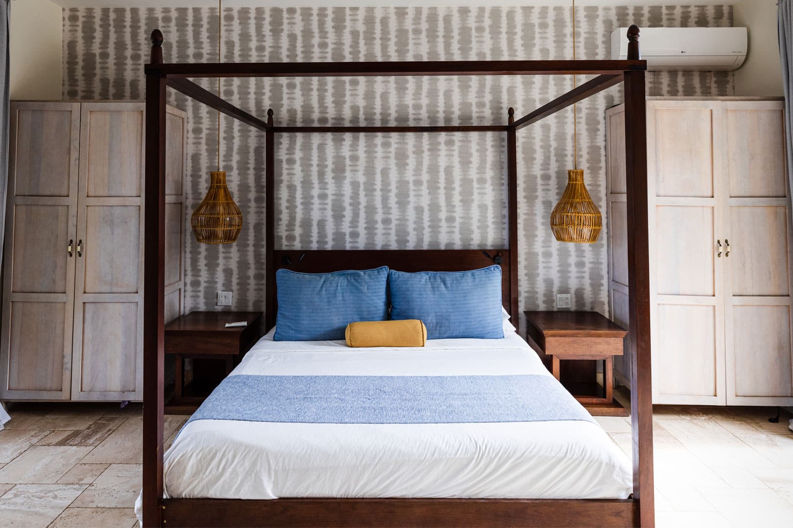 Master bedroom with a bed that has pillows and linen, two side tables and two identical white closets on each side inside of the Seafront Suite at The Lodge at Jaguar Reef Resort