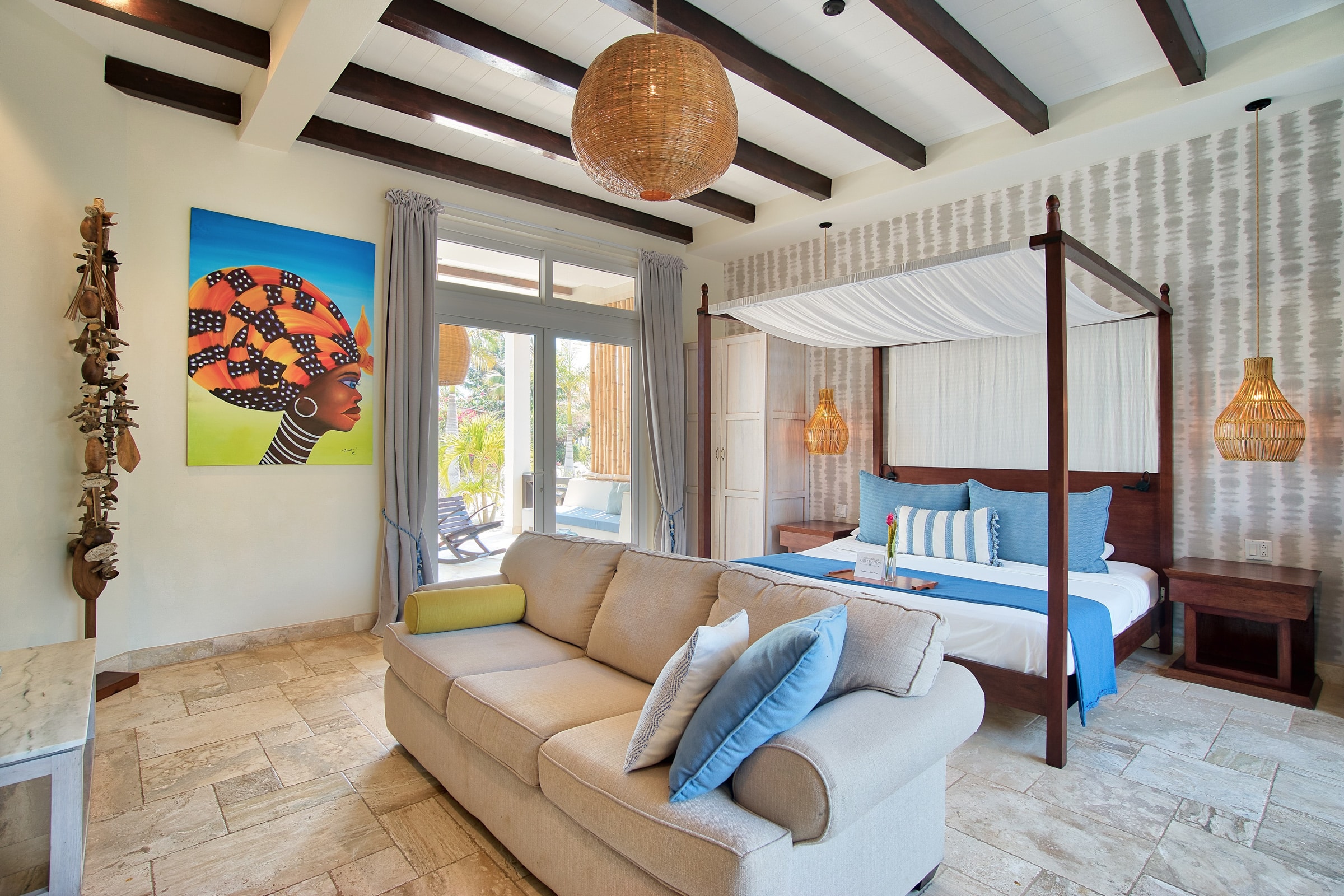 Living room area with a couch, bed, side table and wall art inside of the Deluxe Suite Lower Level with Plunge Pool at The Lodge at Jaguar Reef Resort