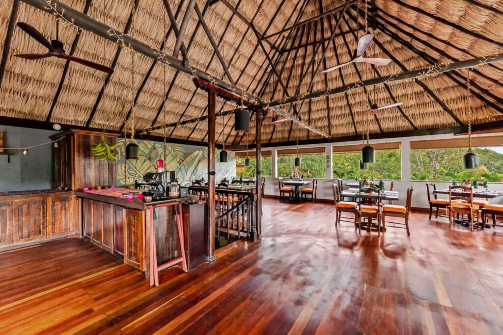 Open-air meeting and event space with wooden floors surrounded by a lush green forest at Sleeping Giant Rainforest Lodge.